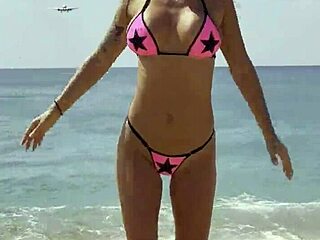Monika Fox poses seductively in pink bikini on sunny beach.